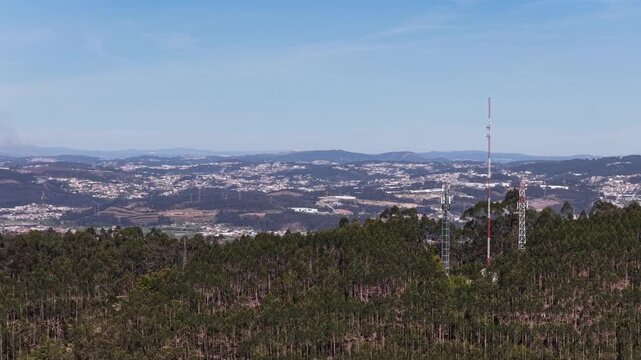 Aerial view of towers peaking over lush green trees, with a sprawling city nestled in the distance, under a soft blue sky, Valongo, Portugal.