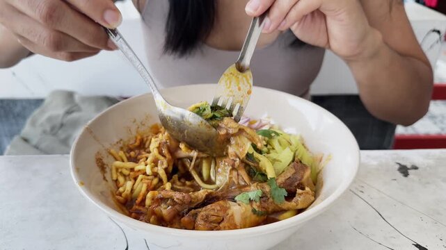 Woman eating Thai food Khao Soi curry noodle soup in Thailand street food restaurant, traditional northern Thai cuisine with noodles and rich broth