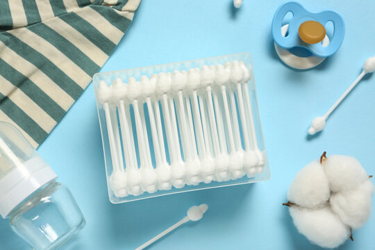 Container with cotton buds, flower, baby pacifier, clothes and bottle on blue background