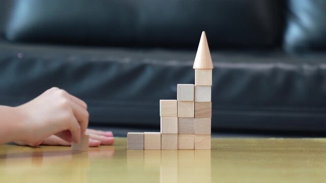 A child places the final wooden block on a rising staircase structure symbolizing steady growth, progress, and reaching new levels step by step.