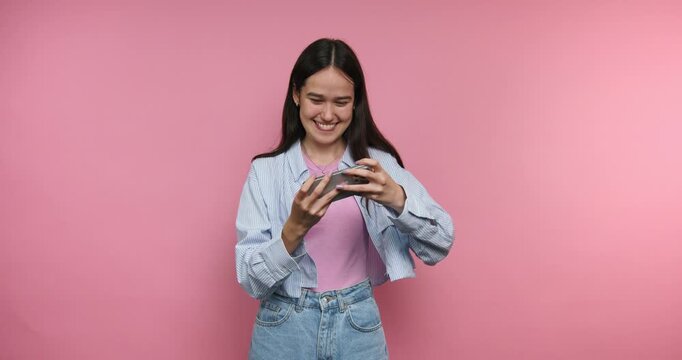 Young woman reacts with joy while using her smartphone in front of a pink background during daylight