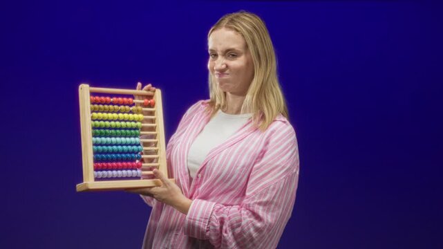 Woman holding abacus, hand gripping wooden frame, pursed lips expression in studio; frustration learning struggle.