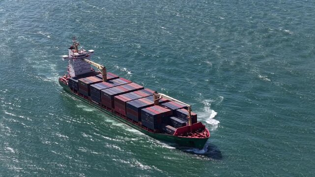 Lisbon, Portugal - 30 March 2026: Aerial view of a container ship sailing across the vast ocean, its hull cutting through the water, leaving a frothy wake.