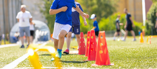 School Sports Class For Kids. Youth Soccer Agility Training. Kids Running Through Cones During Football Practice on Grass Field