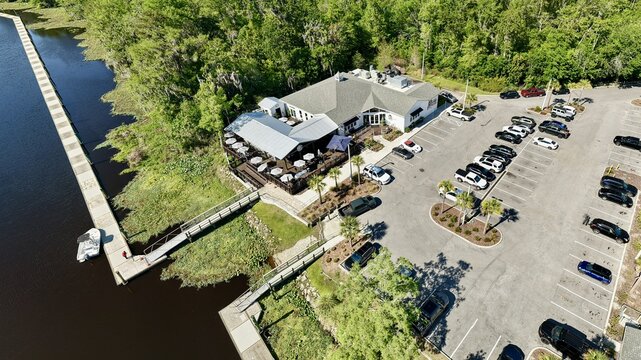 Aerial view of a restaurant with outdoor seating and a dock on the water, a vivid contrast of dark water and lush greenery, St. Augustine, Florida, United States.