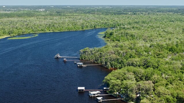 Aerial view of the dark, winding river contrasting with the vibrant green forest and docks along Palmo Fish Camp Road, St. Augustine, Florida, United States.
