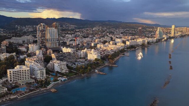Aerial drone view of modern high rise buildings in Limassol illuminated by warm golden hour sunlight with mountains in the background