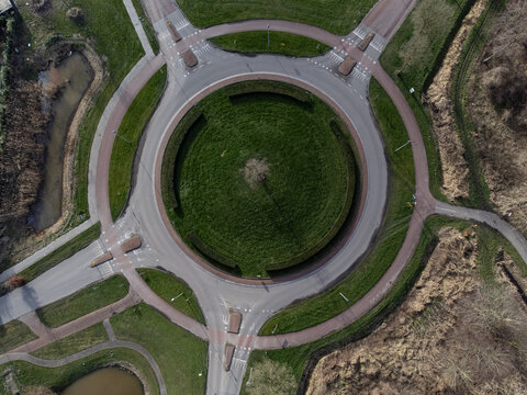 Aerial view of a roundabout with a circular green grass area in the center, surrounded by gray roads and green grass, Overgooi, Flevoland, Netherlands.