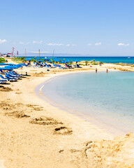 Obraz premium Crystal clear turquoise sea in a small rocky bay near Fig Tree Beach in Protaras, Cyprus on a sunny summer day. Calm shallow water, sandy shoreline and copy space create a perfect travel and vacation 