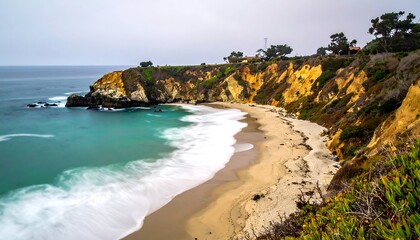 Fototapeta premium Coastal scene shows turquoise water washing against a sandy beach, with a rocky cliff edged with vegetation in view