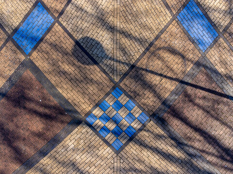 Aerial view of a patterned brick ground surface with a combination of earth-toned and blue tiles, casting tree shadows, Maastrichtkwartier, Flevoland, Netherlands.