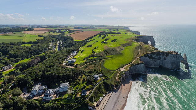 Aerial view of the dramatic cliffs meeting the turquoise sea, lush green golf courses contrasting with the white chalk formations, Etretat, Normandy, France.