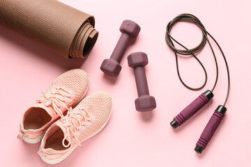 Obraz premium Yoga mat with brown dumbbells, skipping rope and shoes on pink background