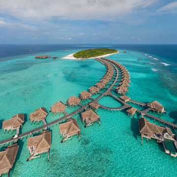 Aerial view of a turquoise dreamscape unfolds with overwater bungalows dotting the vibrant seascape near a verdant island, Male, Male, Maldives.