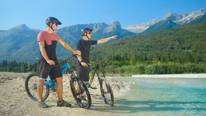 Fototapeta premium Guys riding bicycles talking and planning their route while standing by river.