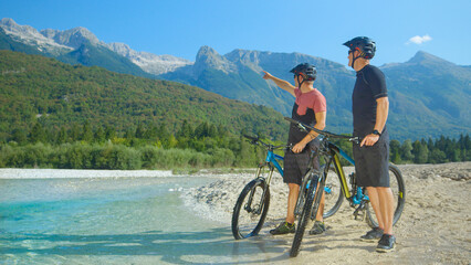 Fototapeta premium Cross country bikers stand by a stream and look around the picturesque nature.