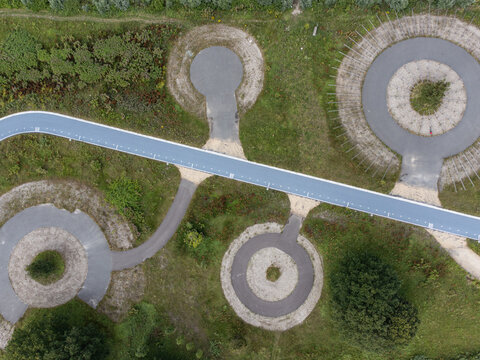 Aerial view of geometric patterns and interconnected circular structures, bisected by a slender blue pathway cutting through the landscape, Utopia, Flevoland, Netherlands.