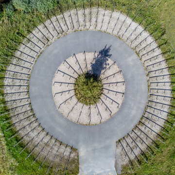 Aerial view of a circular structure with radiating lines, a central green patch casting a dark shadow, contrasted against surrounding grass, Utopia, Almere, Netherlands.
