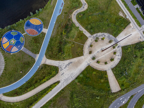 Aerial view of a sundial and colorful circular designs amidst green fields and concrete paths, Utopia, Flevoland, Netherlands.