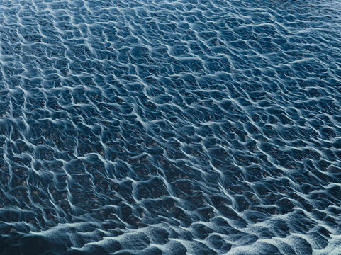 Aerial view of dark, sandy terrain etched with delicate, frost-kissed rivulets creates an intricate tapestry of shadow and light, Iceland, Iceland.