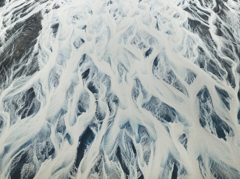 Aerial view of glacial rivers carve intricate patterns across the stark landscape, a symphony of icy blues and earthy browns creating a mesmerizing abstract masterpiece, Iceland, Iceland.