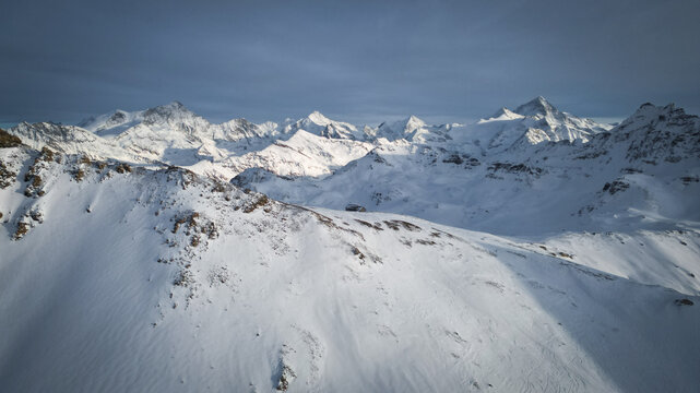 Aerial view of snow-capped peaks piercing the sky, a pristine white canvas etched with shadows and sunlight, creating a majestic winter panorama, Anniviers, Valais, Switzerland.