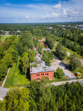 Aerial view of historic red-brick buildings nestled amidst a sea of lush green trees, creating a striking contrast between the man-made structures and the vibrant natural landscape, Liepaja, Latvia.