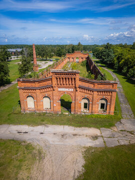 Aerial view of weathered red brick fortress embracing history amidst green trees, under a vast blue sky, Liepaja, Latvia.