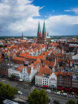 Aerial view of the striking twin spires of the Marienkirche rise above the old town's red-tiled roofs, framed by a vibrant sky, Lubeck, Schleswig-Holstein, Germany.