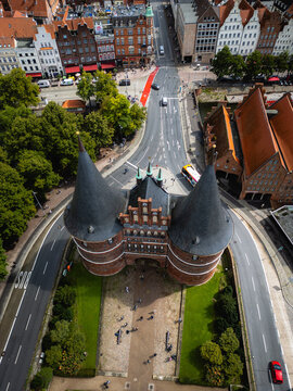 Aerial view of the iconic Holsten Gate standing proudly amidst the bustling streets and verdant parks, its dark spires contrasting with the bright cityscape, Lubeck, Schleswig-Holstein, Germany.