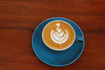 Top view of latte art coffee in blue cup placed on wooden table with clean aesthetic composition.