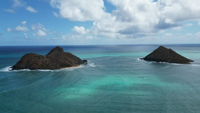 Aerial view of the tranquil turquoise waters surrounding the rugged, dark islands under a bright, scattered cloudscape, Kailua, Hawaii, United States.