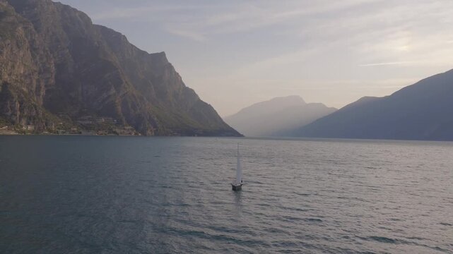 Pull back drone shot of a sailing boat at sunrise on lake Garda in Italy , mountain in the background beautiful lighting 4K 60fps slow motion possible mavic 4 pro
