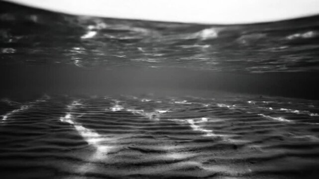 Black and white underwater cinematic view of the ocean floor, showcasing waves in the sand with light and shadows