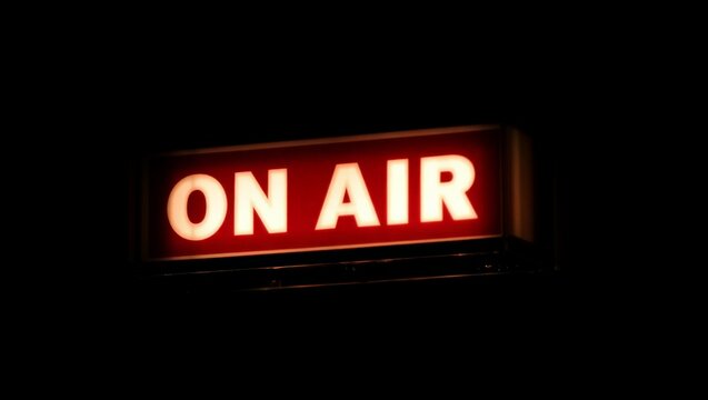 A bright red ON AIR sign indicating a live radio or podcast broadcast in a dark studio or setting.