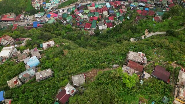 Aerial reveal of scenic hillside barangay village homes with colorful rooftops and lush greenery - Valley of Colors, Philippines