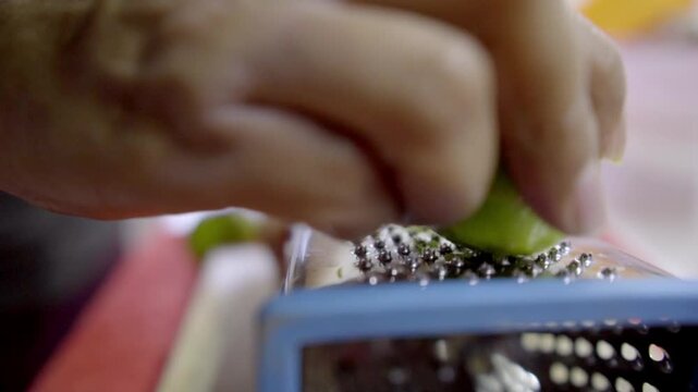 Close-up of hands grating lime in kitchen for food preparation