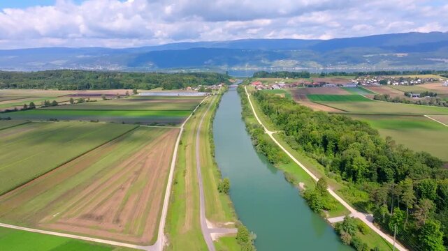 Smooth drone flight along the Hagneck Canal after the bridge, heading directly toward the village of Hagneck across green fields in the Swiss Seeland region.
