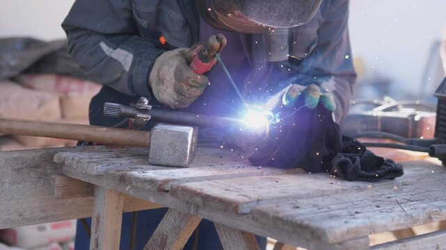 Welder Welding Metal Joint With Arc. Protective Helmet And Thick Gloves, Bright Blue Arc And Sparks Illuminate Rugged Workshop Bench, Torch Guided By Experienced Tradesman Fusing Joint,