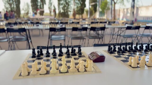 Chess boards with clocks at tournament hall, no people visible. Focus on game setup with blurred background of multiple tables, strategy and competition concept.