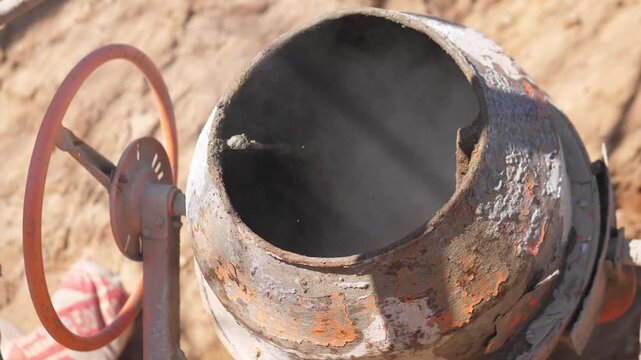 Concrete Mixer Drum Turning On Site Rusted Metal Drum Rotating While Shovel Deposits Sand And Cement, Wet Mix Stirring Inside, Closeup Texture Of Plaster And Gritty Aggregate, Sunlit Outdoor