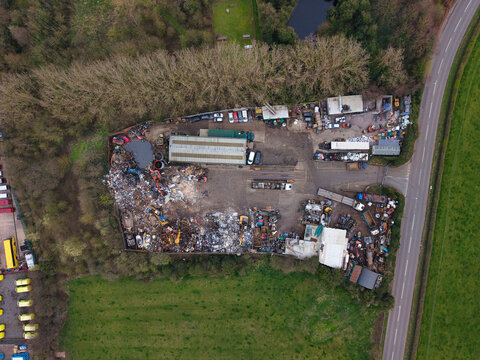Aerial view of a scrap yard filled with metallic debris and colorful refuse near a road and a patch of trees, Stafford, England, United Kingdom.