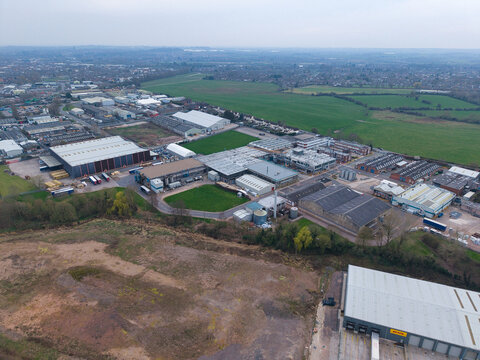 Aerial view of industrial buildings nestled near fields, a blend of gray structures and green spaces under an overcast sky, Redditch, United Kingdom.