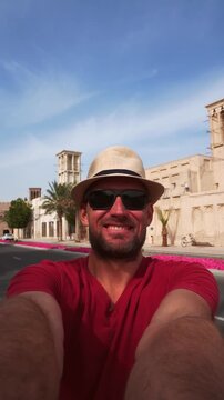A happy tourist wear red shirt and straw hat takes selfie at the Al Fahidi Historical Neighborhood in Old Dubai. Features a traditional wind tower backdrop cityscape view