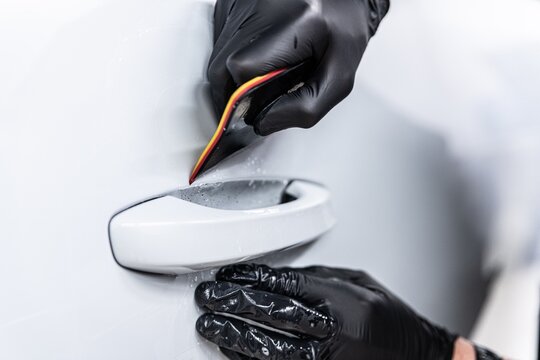 Close-up of a detailer applying paint protection film (PPF) around a car door handle. This area is highly prone to scratches, and the film provides durable protection against daily wear.