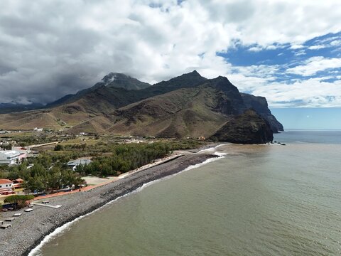 Aerial view of the rugged coastline meeting the vast ocean under a sky of contrasting clouds, Puerto de la Aldea, Canarias, Spain.