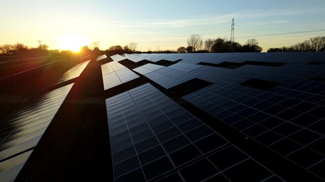 Aerial view of a solar farm bathed in the warm glow of the setting sun, casting long shadows across the panels, Tye Lane, Ipswich, United Kingdom.