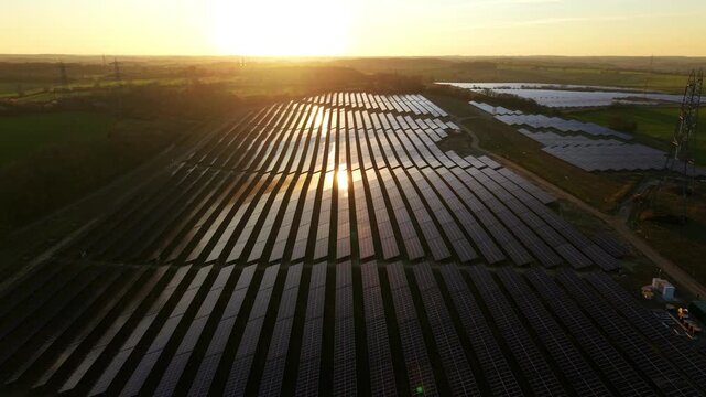 Aerial view of the Tye Lane Solar Farm as the golden sun reflects off the panels, creating a mesmerizing contrast against the green landscape, Ipswich, United Kingdom.