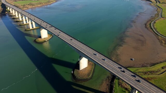Aerial view of the Orwell Bridge stretching across the vibrant blue waters, connecting lush green landscapes under a clear sky, Ipswich, England, United Kingdom.
