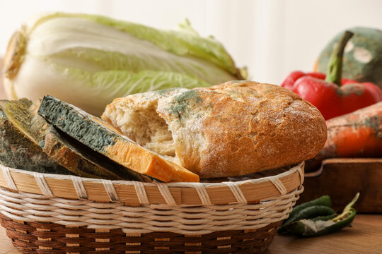 Wicker basket with moldy vegetables, cheese and bread on counter in kitchen